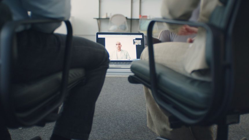 Duas pessoas acompanham uma consulta on-line em um laptop, em um ambiente profissional.