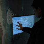 Silhueta de uma pessoa interagindo com um mapa digital em uma tela sensível ao toque, em ambiente escuro.