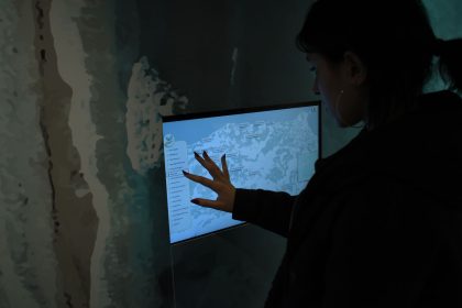 Silhueta de uma pessoa interagindo com um mapa digital em uma tela sensível ao toque, em ambiente escuro.