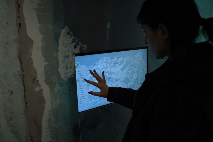 Silhueta de uma pessoa interagindo com um mapa digital em uma tela sensível ao toque, em ambiente escuro.