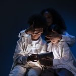 Mãe supervisiona duas crianças enquanto usam um tablet em ambiente doméstico.