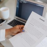 Pessoa segura um documento jurídico ao lado de um laptop durante uma sessão de trabalho.
