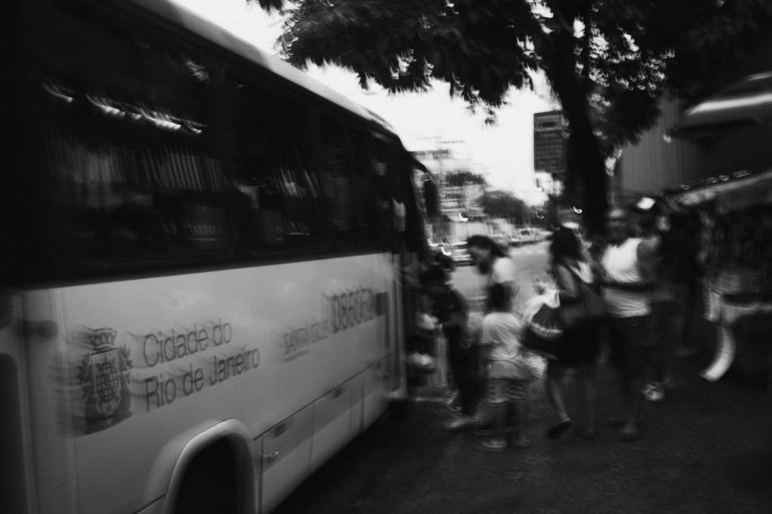 Pessoas embarcam em um ônibus urbano no Rio de Janeiro, em uma fotografia em preto e branco.