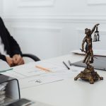 Mesa de trabalho jurídico com documentos, um notebook e uma estatueta da Justiça.