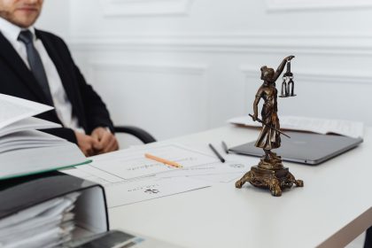 Mesa de trabalho jurídico com documentos, um notebook e uma estatueta da Justiça.