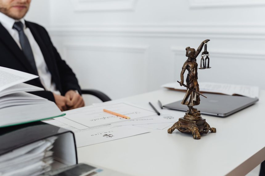 Mesa de trabalho jurídico com documentos, um notebook e uma estatueta da Justiça.