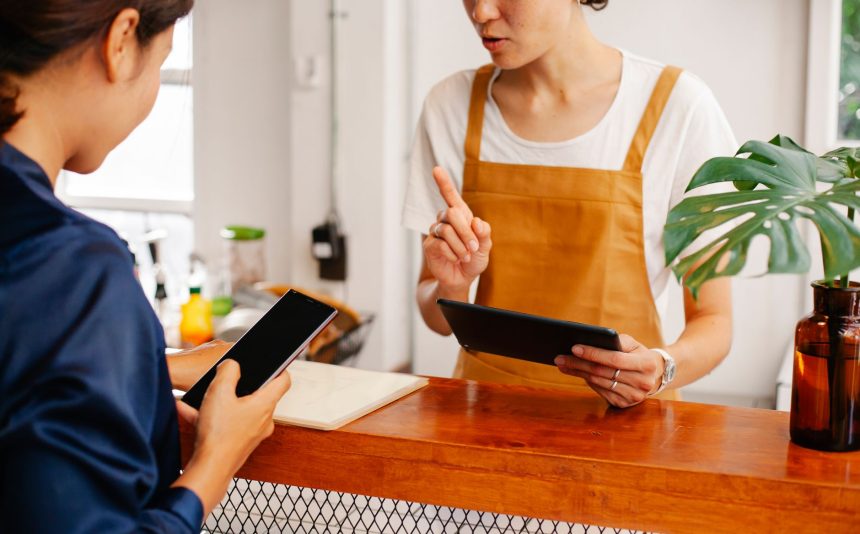 Duas pessoas conversam enquanto uma delas toca a tela de um celular em um ambiente de atendimento.